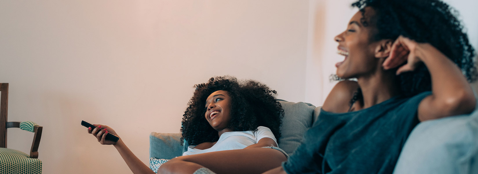 Two black women relax in their hotel room and watch TV from DIRECTV on SONIFI's interactive system