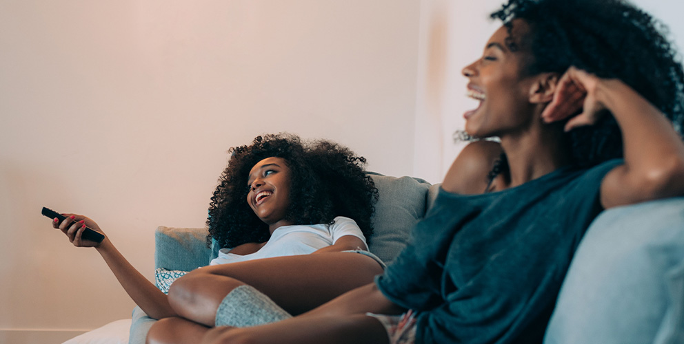 Two black women relax in their hotel room by watching an on-demand movie on SONIFI's interactive TV platform