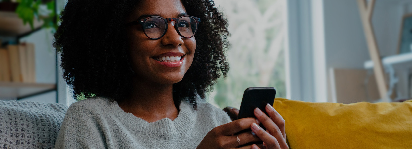 A black woman with glasses holds her mobile phone while watching TV on SONIFI's interactive platform in her hotel room