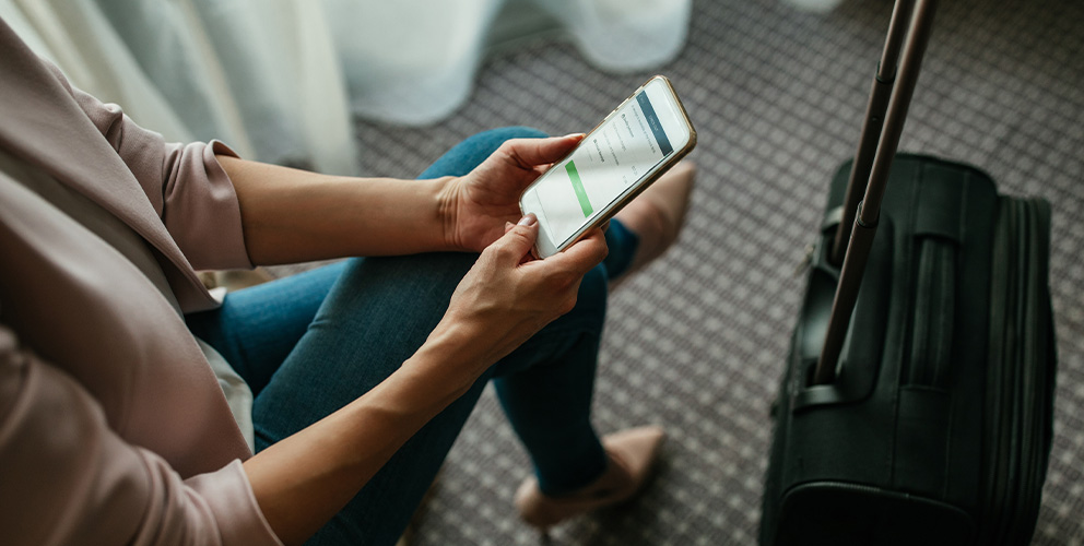 A person sits next to a suitcase and uses their mobile phone to check out of their hotel room using SONIFI's smart mobile controls