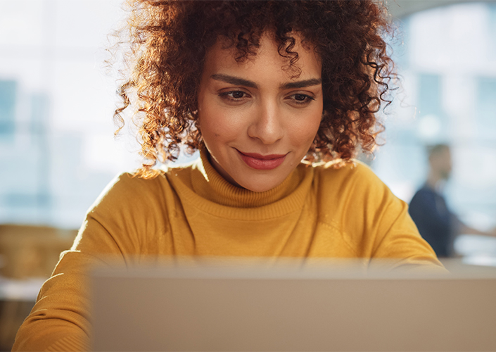 A woman in a yellow shirt is working on her laptop to access Event Manager from SONIFI to create custom internet networks for hotel conferences and events