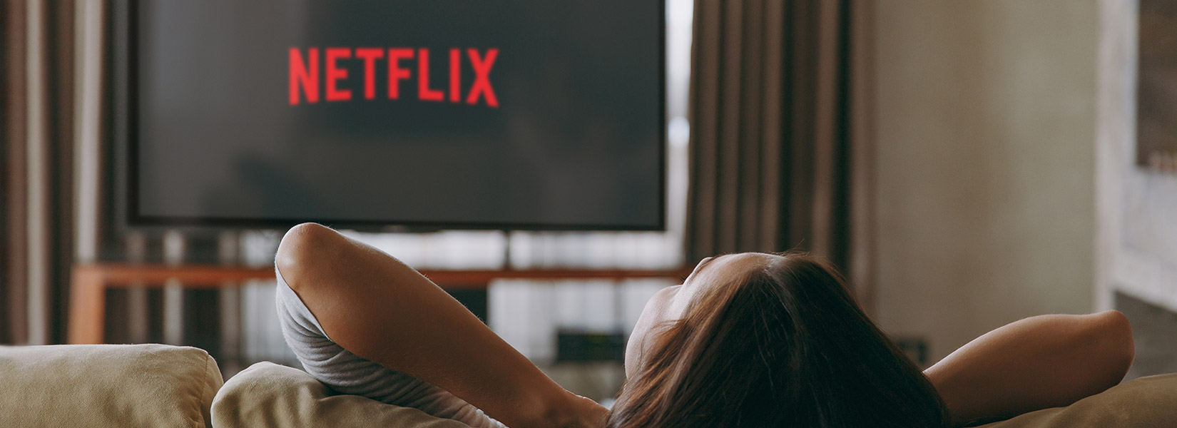 A person relaxes in their hotel room while watching Netflix on the TV using SONIFI's STAYCAST solution