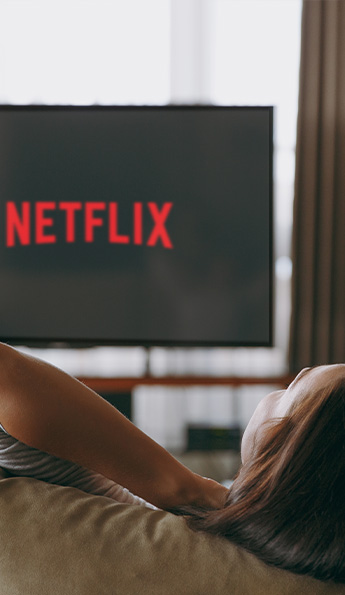 A woman relaxes on a couch streaming Netflix on a hotel room TV.